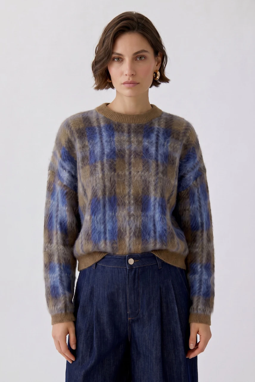 Casual women's pullover: Woman in a blue and brown plaid pullover with relaxed fit, paired with denim pants.