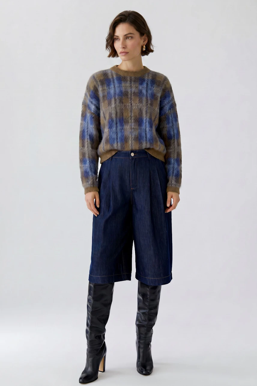 Casual pullover: Woman in plaid pullover with wide-leg jeans and knee-high boots, standing confidently.