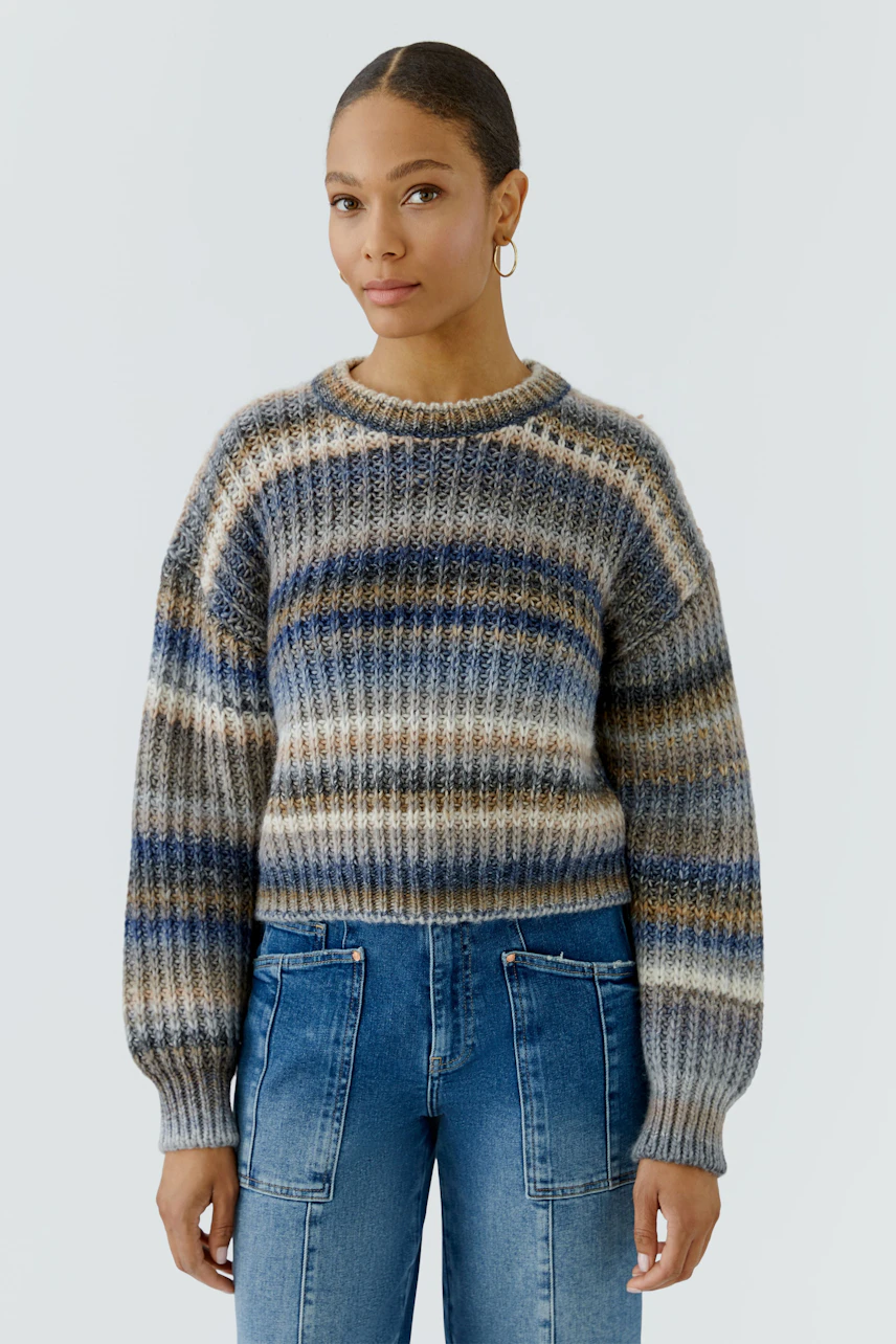 Casual women's pullover: Woman in a striped knit pullover with blue jeans, looking confidently.