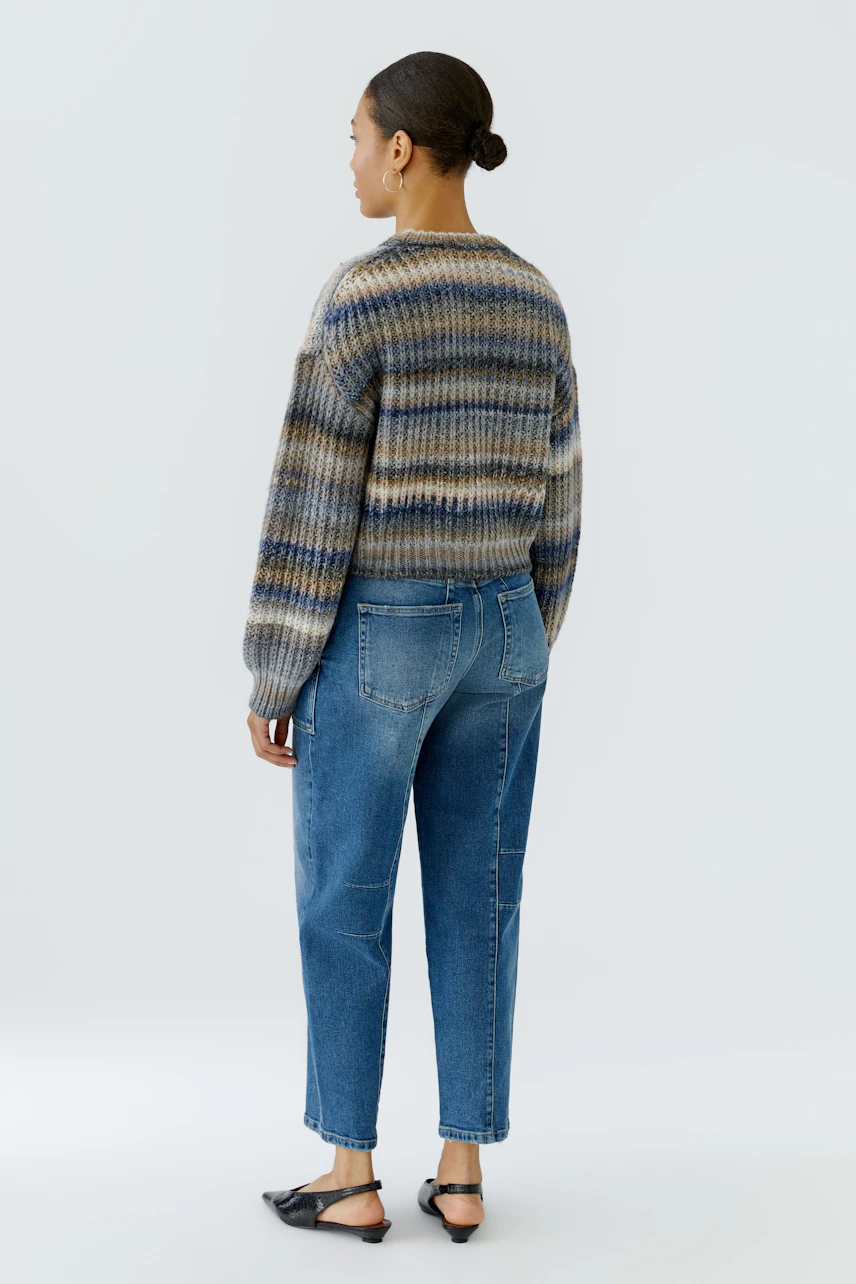 Casual pullover: Woman in a striped knit pullover and blue jeans, standing with a relaxed posture.