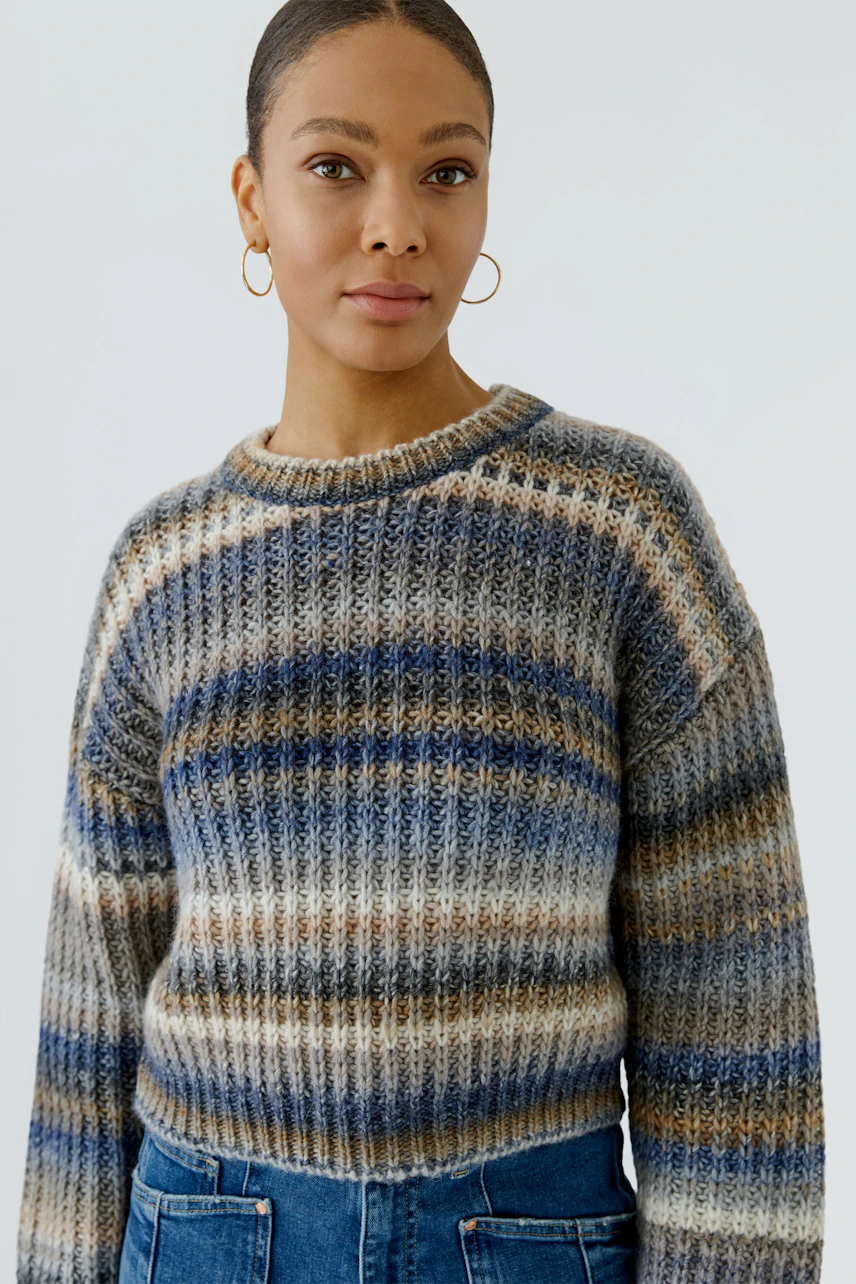 Casual women's pullover: Woman in a striped knit pullover with blue and beige tones, paired with denim jeans.