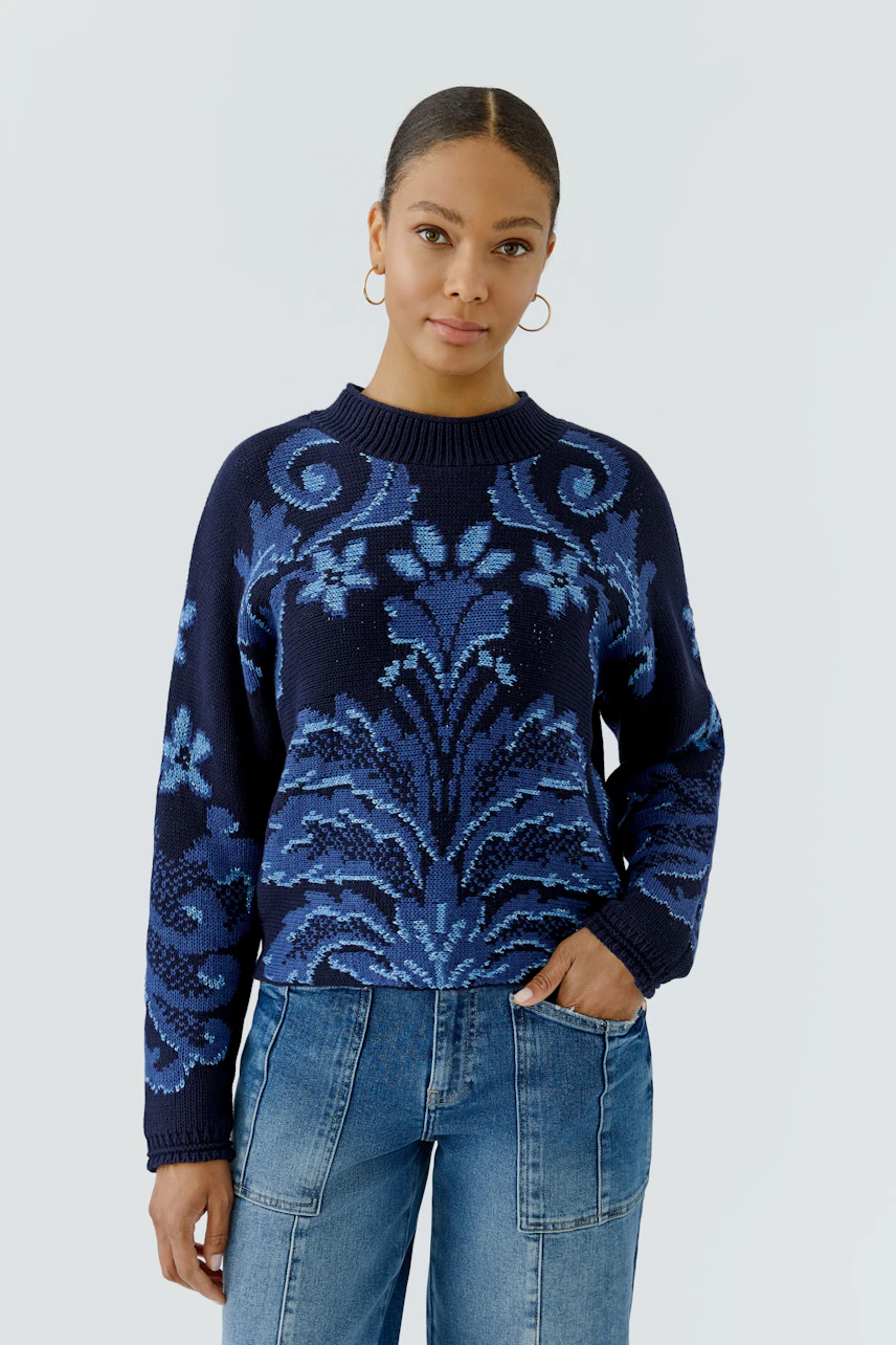 Damen-Pullover: Frau im blauen Pullover mit floralem Muster und Jeans, lässiger Look.