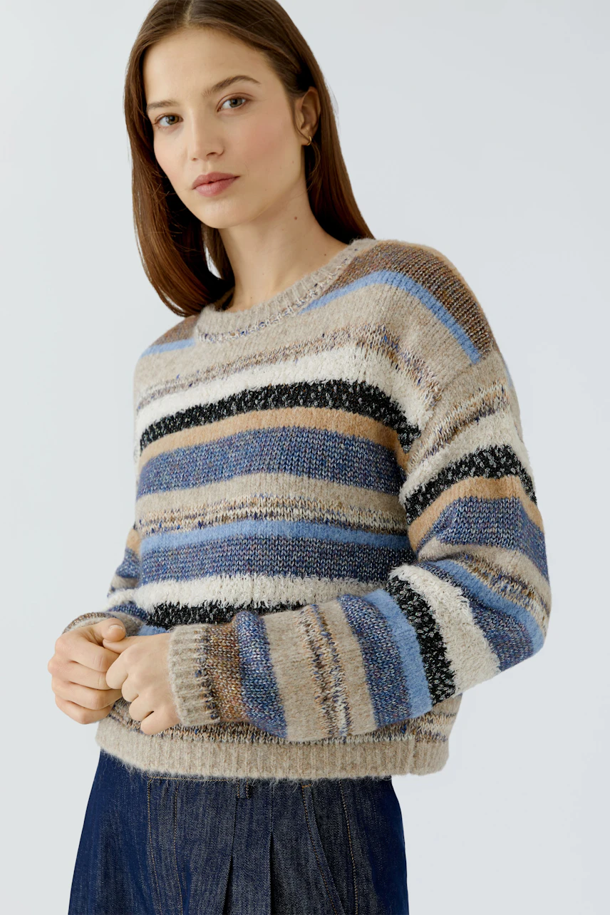 Casual women's pullover: Woman in a striped, textured pullover with blue and brown tones, looking relaxed.