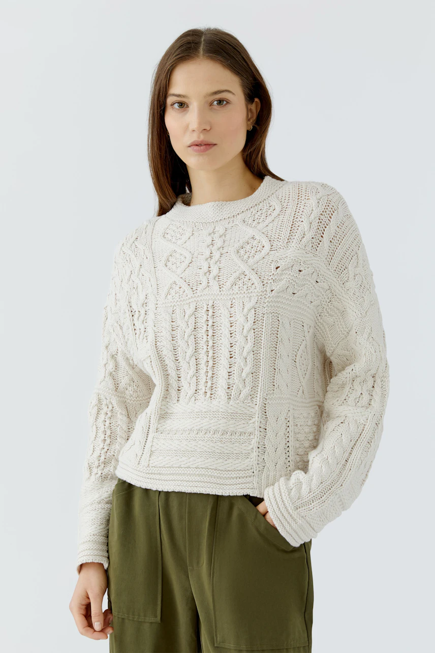 Casual women's pullover: Woman in a white knit pullover with intricate patterns, paired with green pants.