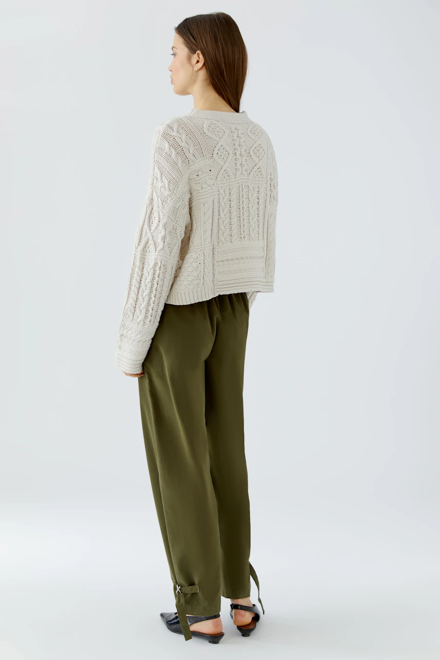 Casual pullover: Woman in a cream knit pullover with textured patterns, paired with olive green pants.
