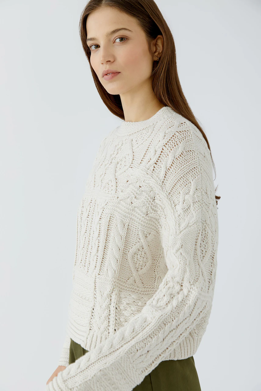 Casual women's pullover: Woman in a cream knit pullover with intricate patterns, paired with olive pants.