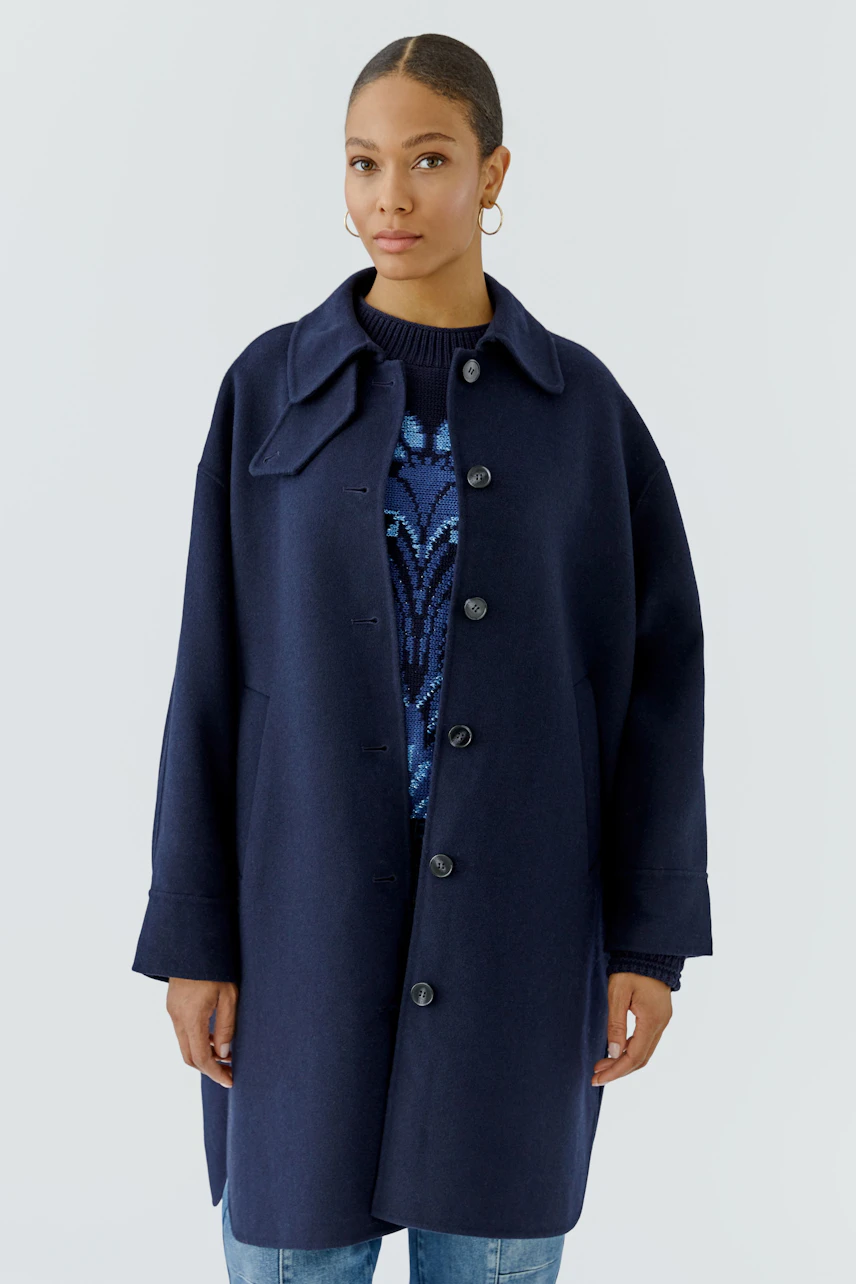 Wool coat: Woman in a navy wool coat over a patterned pullover, paired with jeans, looking poised.