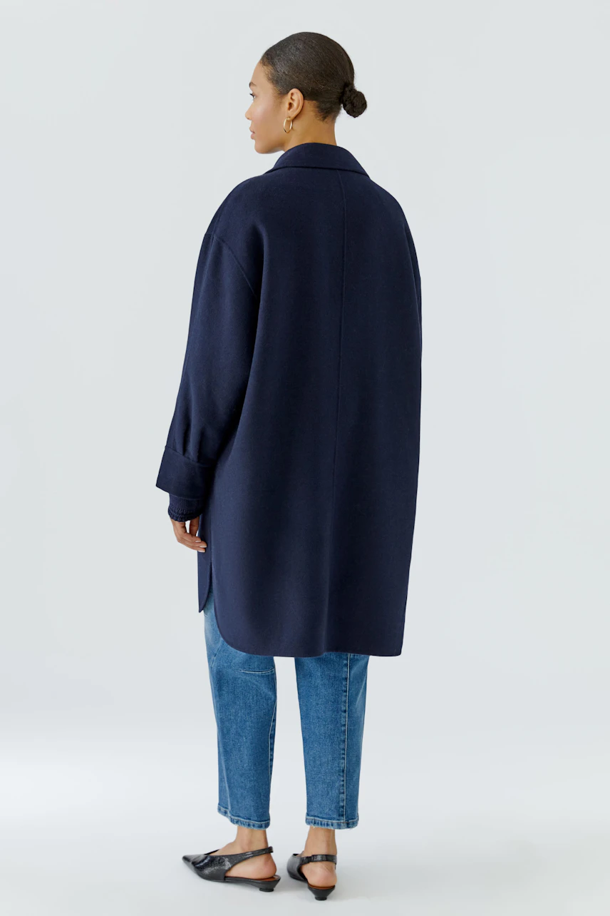 Woman in a navy wool coat, paired with blue jeans and black flats, standing confidently.