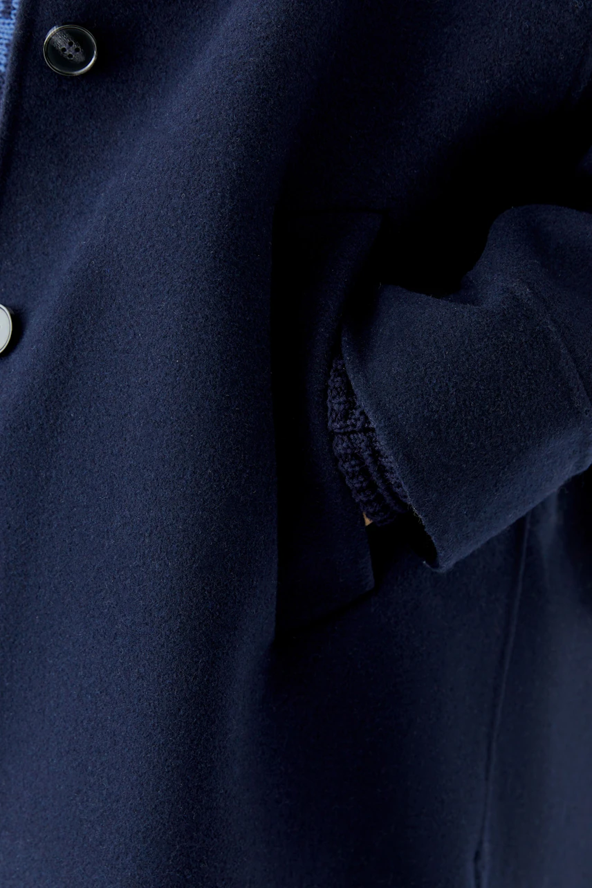 Navy wool coat: Close-up of a woman's hand in pocket, showcasing soft texture and classic button detail.