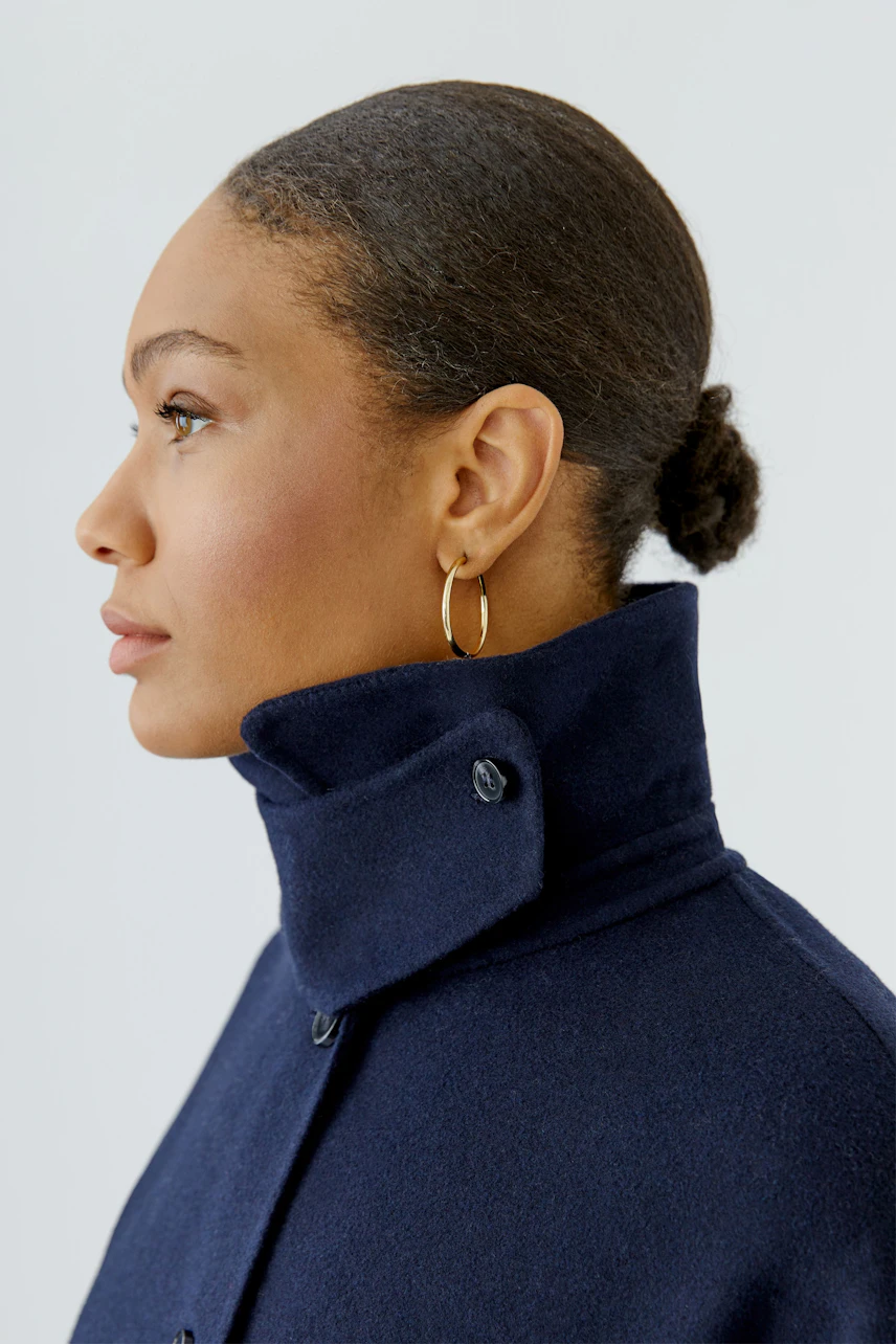 Woman in a navy wool coat with high collar, looking to the side. Simple and stylish outerwear.