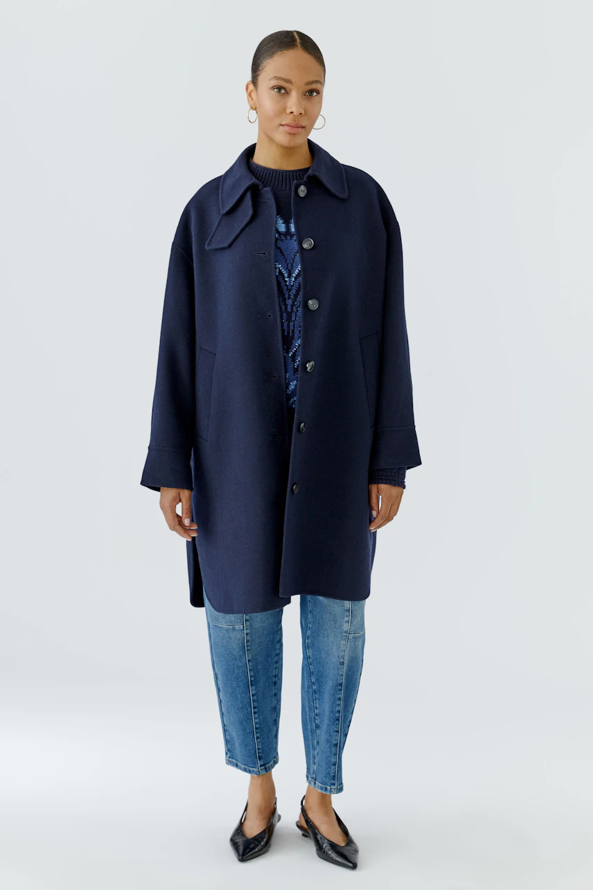 Woman in navy wool coat, buttoned over a patterned pullover, paired with jeans and black flats.