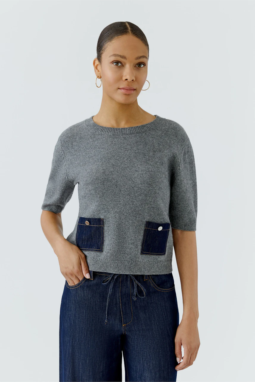 Casual women's pullover: Woman in a gray pullover with denim pockets, paired with dark jeans.