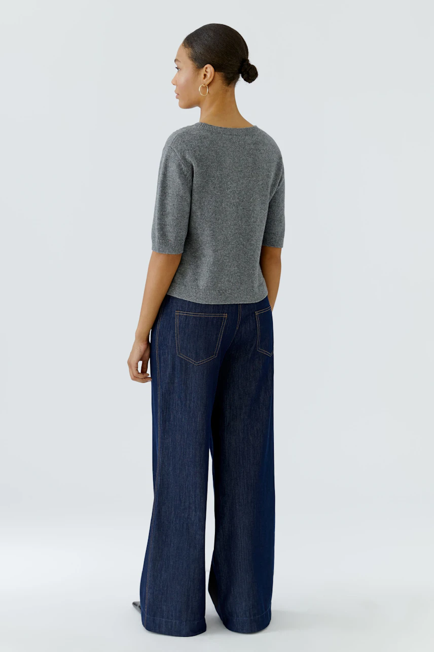 Casual women's pullover: Woman in a grey pullover with short sleeves and wide-leg jeans, seen from the back.