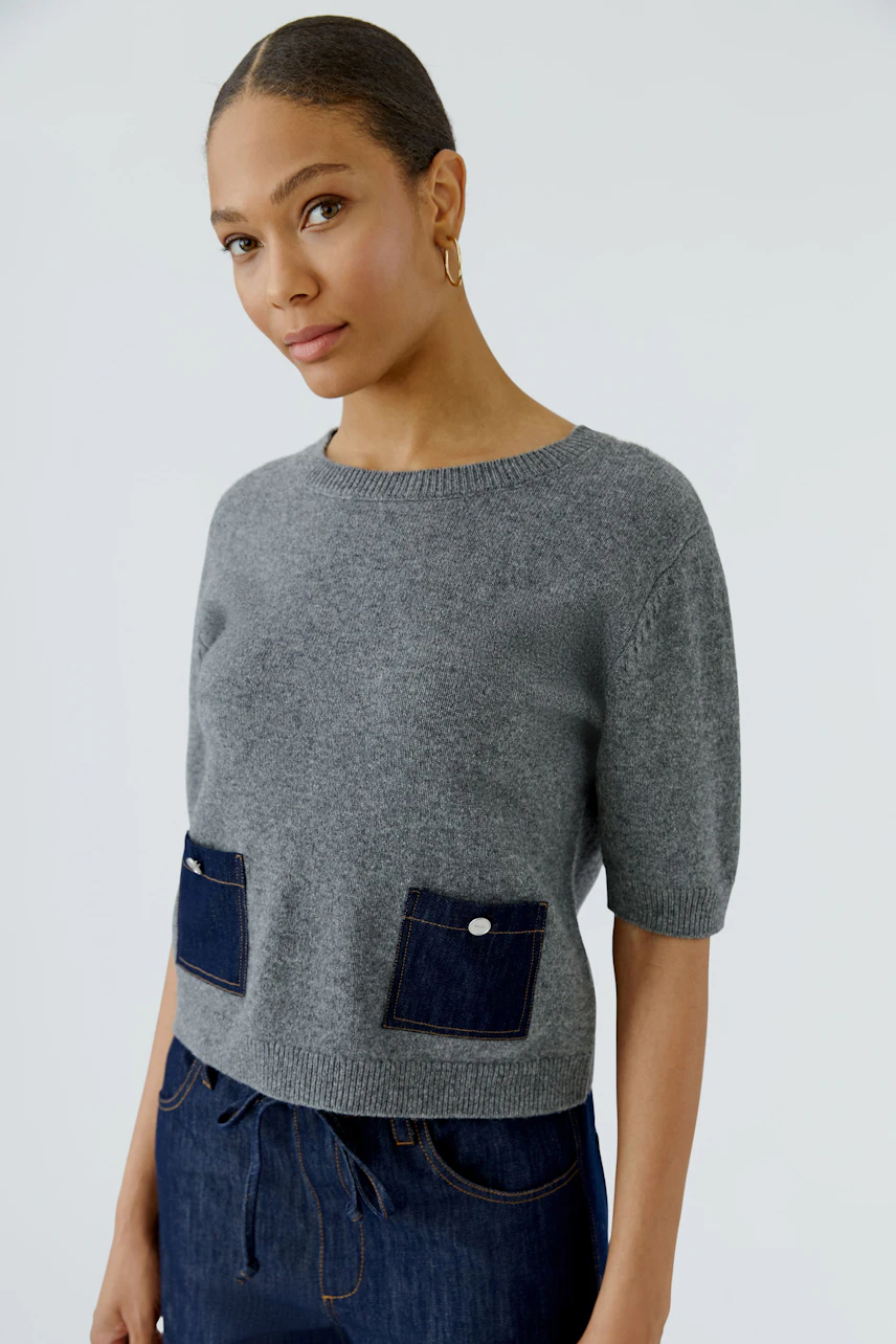 Casual women's pullover: Woman in a grey pullover with denim pockets, paired with dark jeans, looks relaxed.