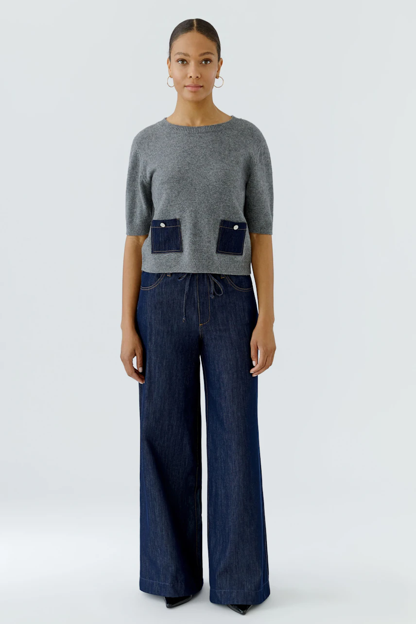 Casual pullover: Woman in a grey pullover with denim pockets, paired with wide-leg jeans, stands confidently.