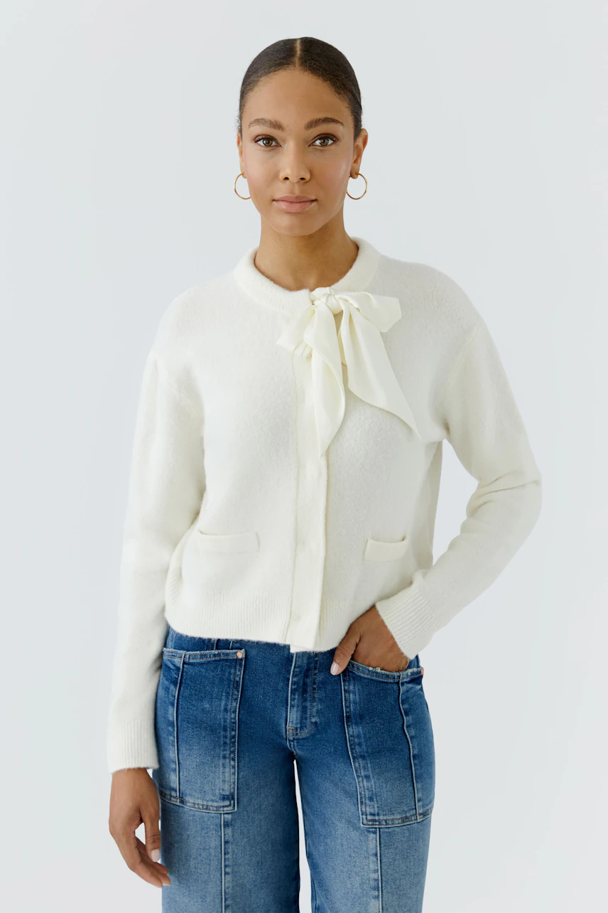 Woman in white cardigan with bow detail, paired with blue jeans. Casual and stylish look.
