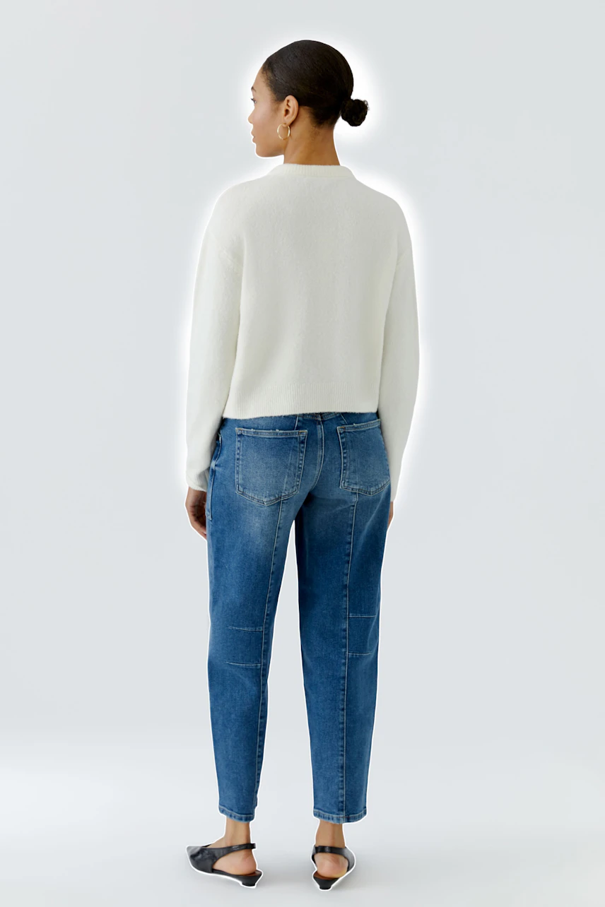 Woman in white cardigan and blue jeans, standing confidently. Casual and stylish look.