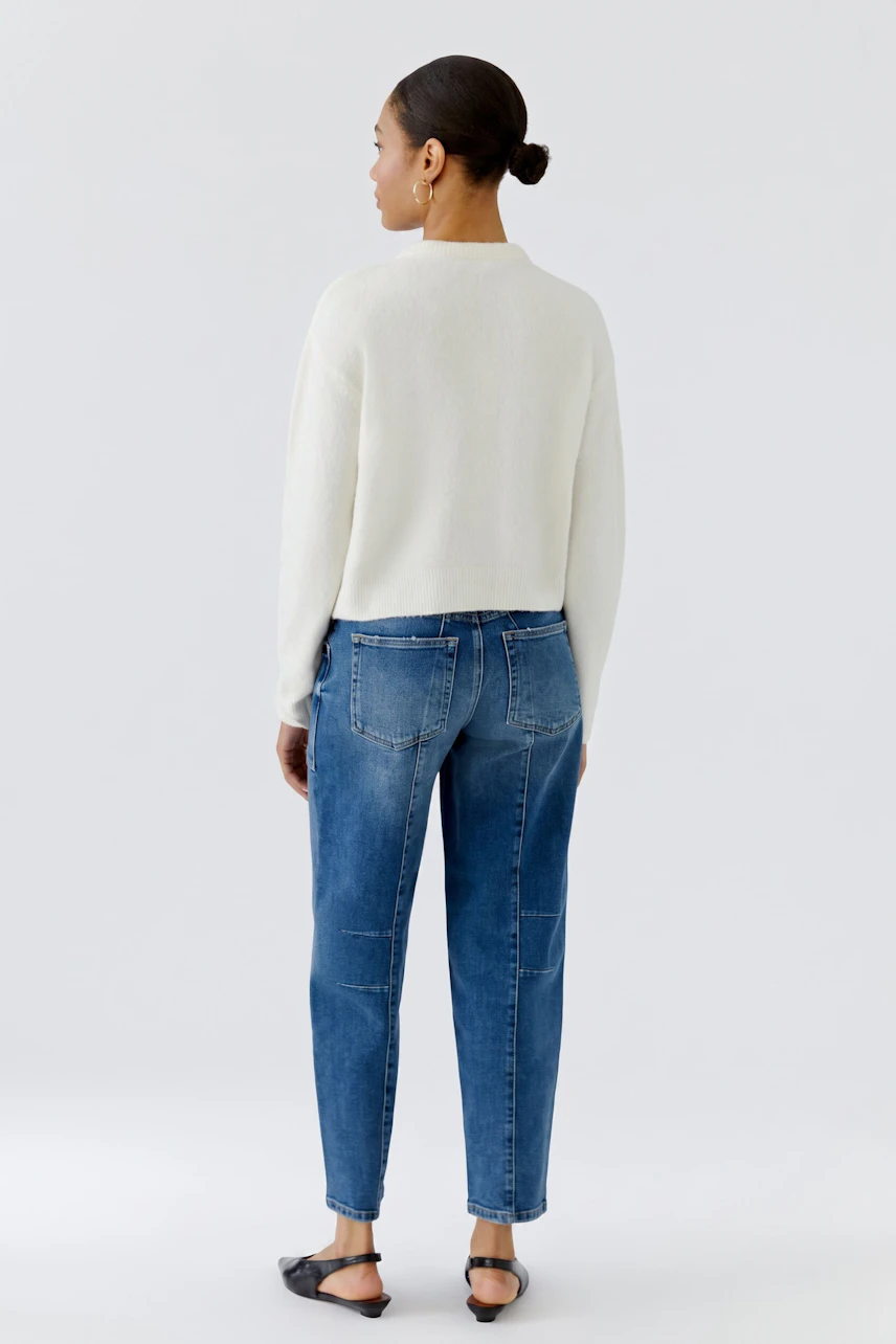 Woman in white cardigan and blue jeans, standing confidently. Casual and stylish look.