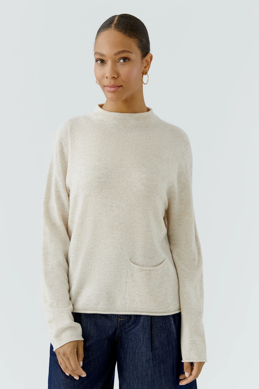 Casual women's pullover: Woman in beige pullover with long sleeves and small pocket, paired with jeans.