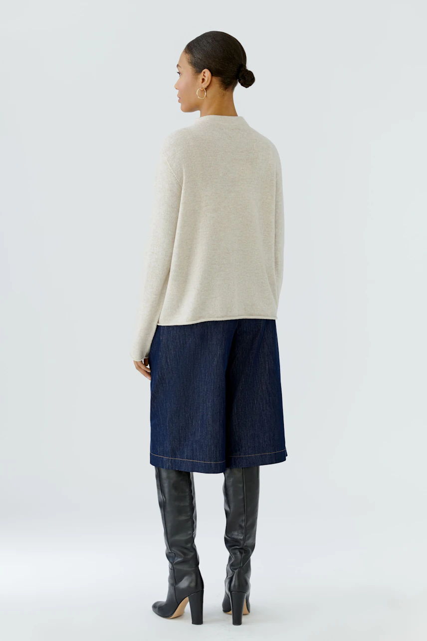 Casual pullover: Woman in beige pullover, denim culottes, and knee-high boots, facing away.