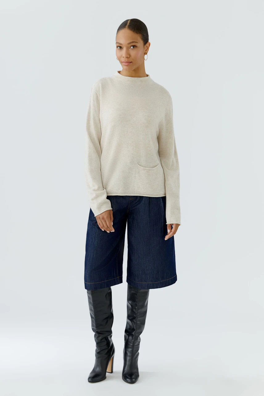 Casual women's pullover: Woman in beige pullover with wide-leg jeans and knee-high boots, standing confidently.