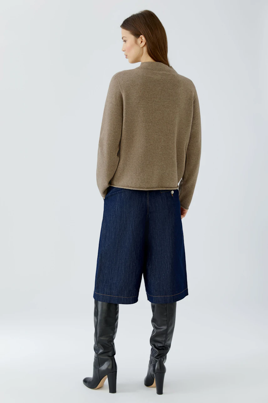 Casual pullover: Woman in a beige pullover, denim culottes, and knee-high boots, viewed from the back.