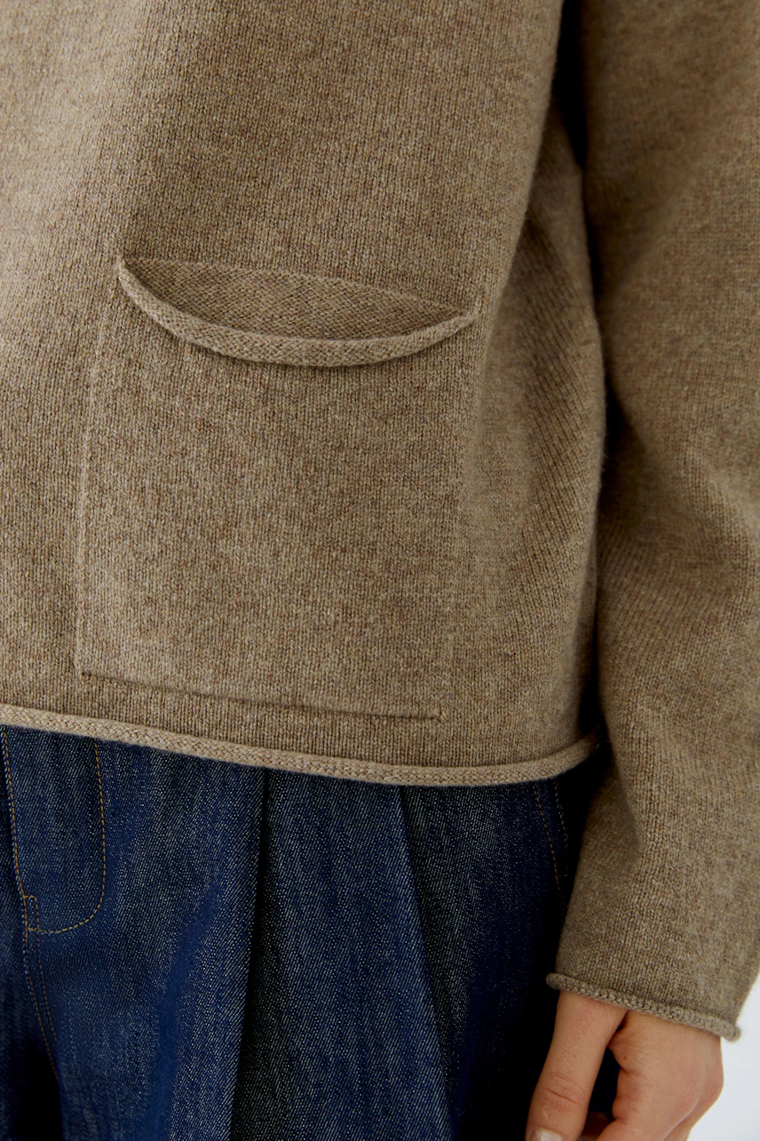 Casual pullover: Woman in a cozy brown pullover with front pocket detail, paired with denim skirt.
