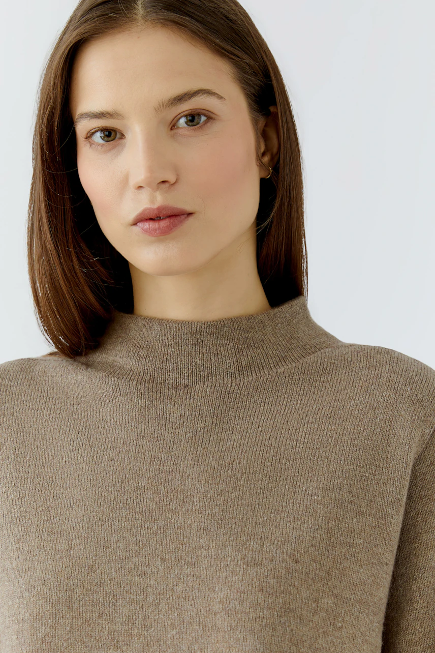Woman in a cozy brown pullover with a high neckline, looking serene.