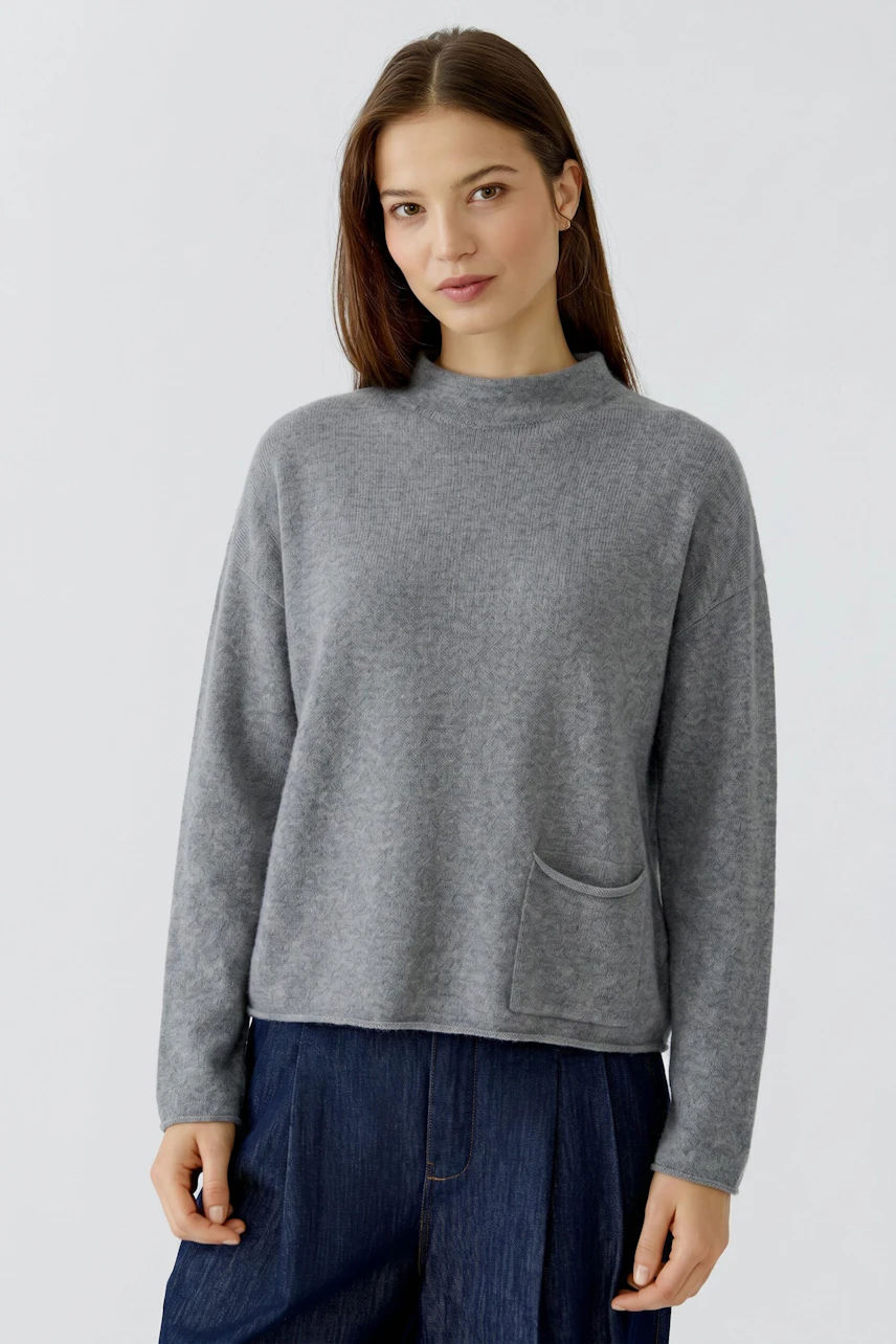 Casual women's pullover: Woman in a grey pullover with a relaxed fit and a front pocket, paired with jeans.