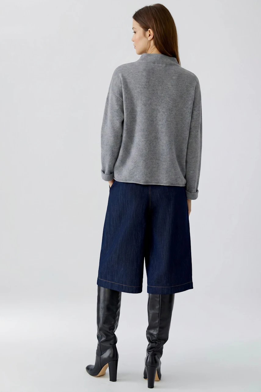 Casual pullover: Woman in a grey pullover, denim culottes, and knee-high boots, viewed from the back.