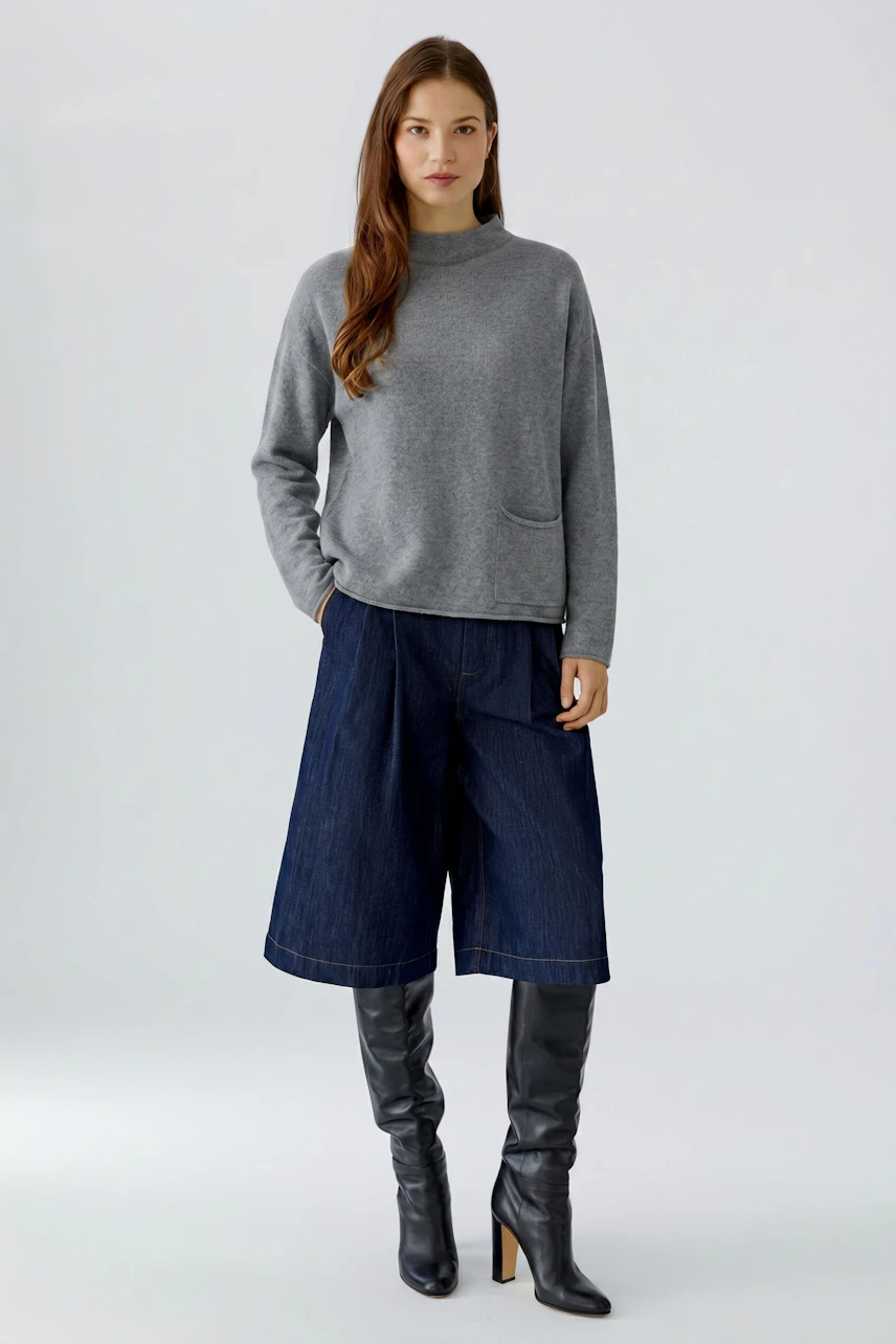 Casual women's pullover: Woman in a gray pullover with wide denim culottes and knee-high black boots.