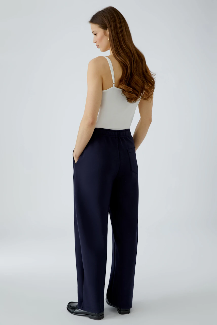 Casual women's pants: Woman in navy wide-leg pants and white tank top, standing with hands in pockets.