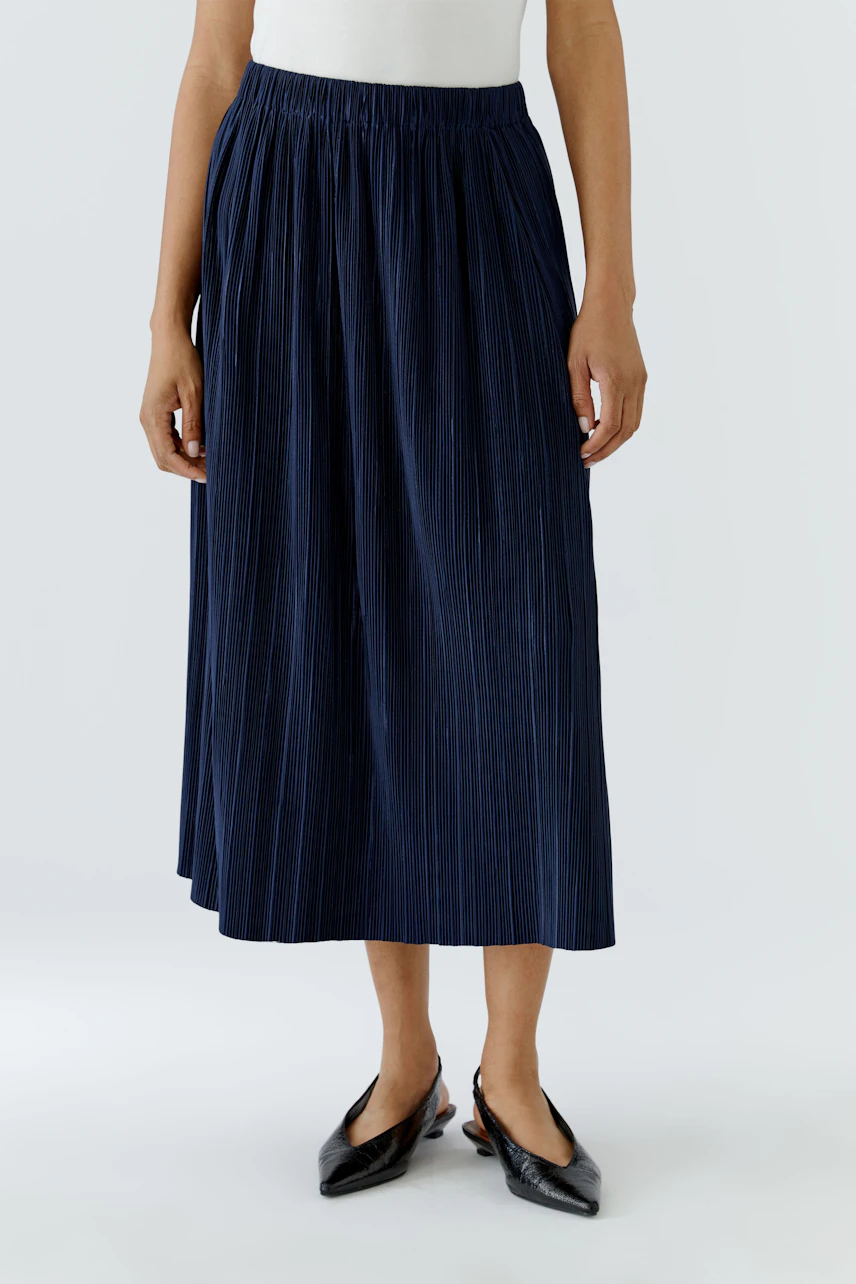 Woman in a navy pleated midi skirt and white top, showcasing a casual and versatile style.