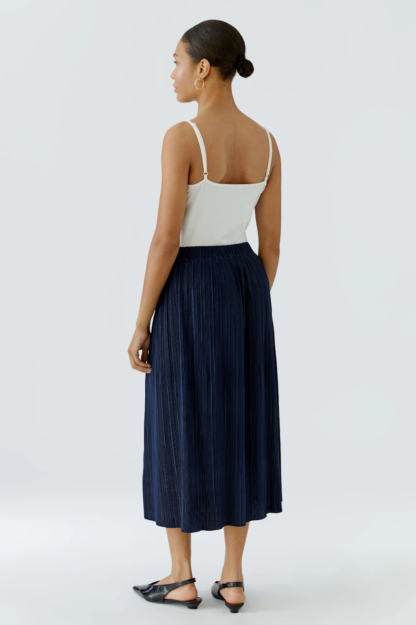 Woman in a navy pleated midi skirt and white top, standing confidently. Casual and stylish look.