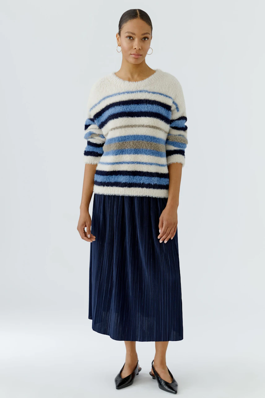 Woman in striped pullover and navy midi skirt, standing confidently.