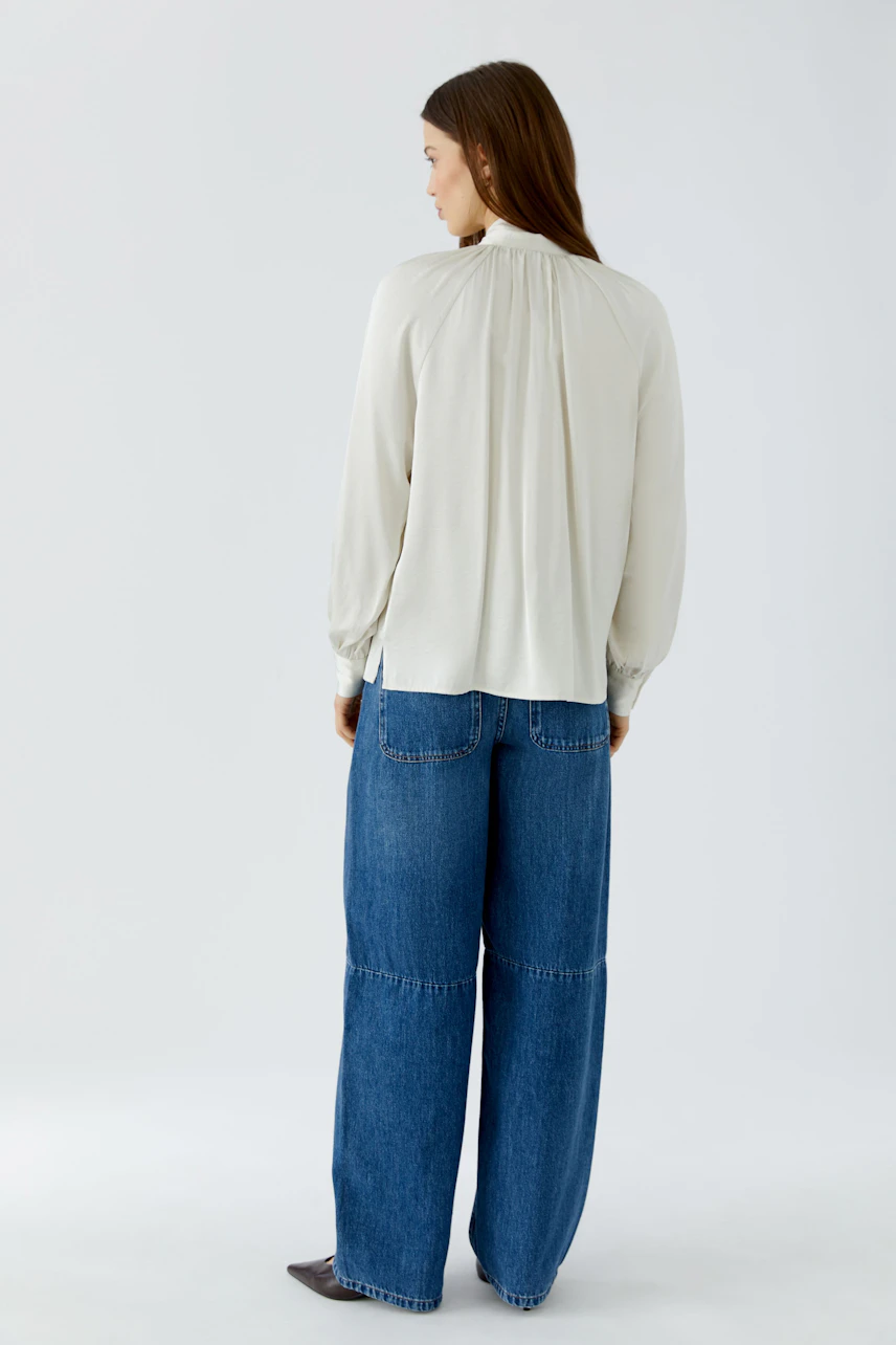 Woman in a white pussy-bow blouse and wide-leg jeans, viewed from the back.