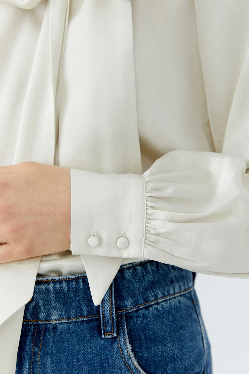 Woman in a white pussy-bow blouse with buttoned cuffs, paired with blue jeans.