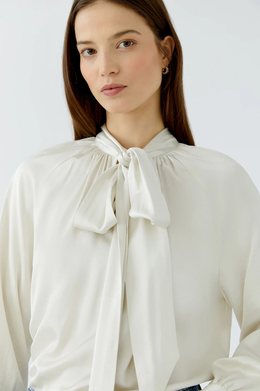 Woman in a white pussy-bow blouse, looking confidently. Simple and stylish design for everyday wear.