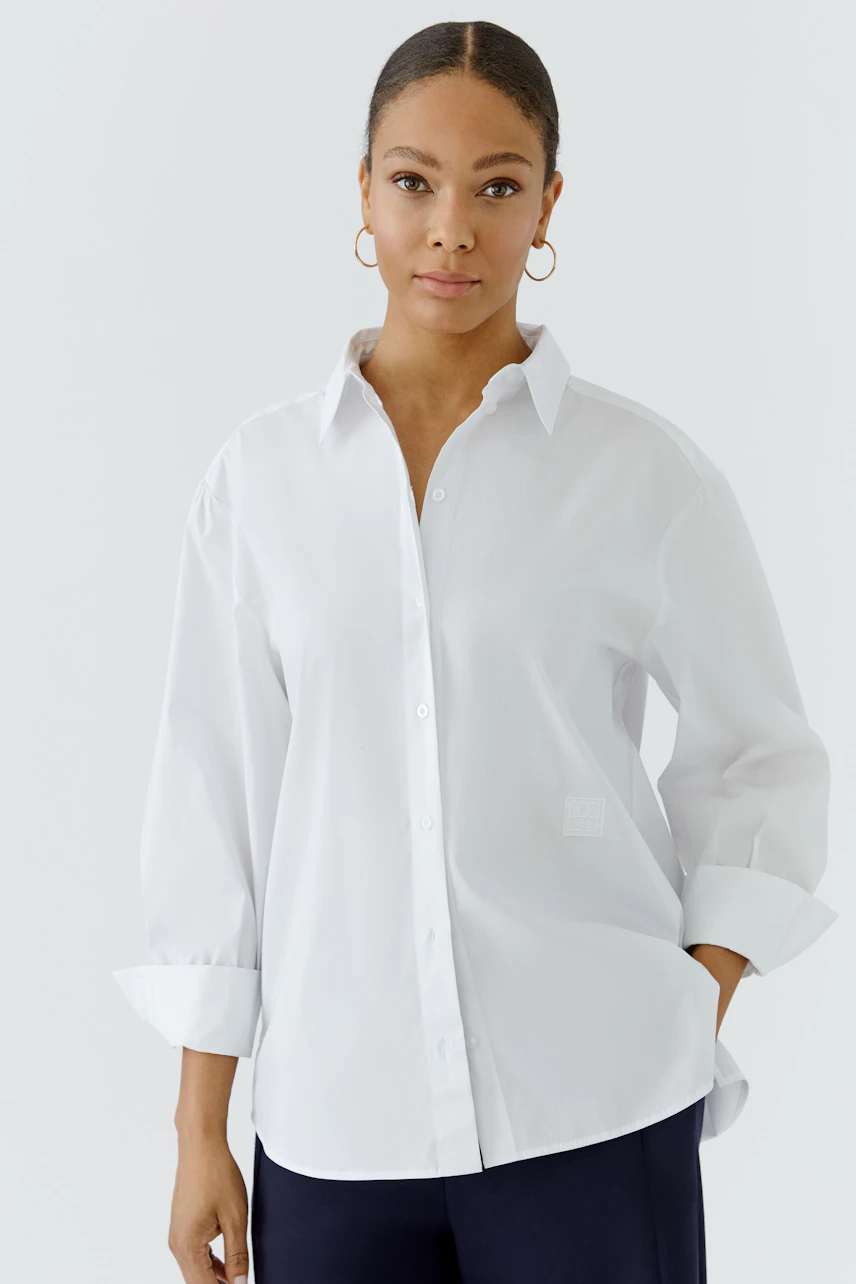 Casual women's shirt blouse: Woman in a white button-up blouse with rolled sleeves, looking confidently.