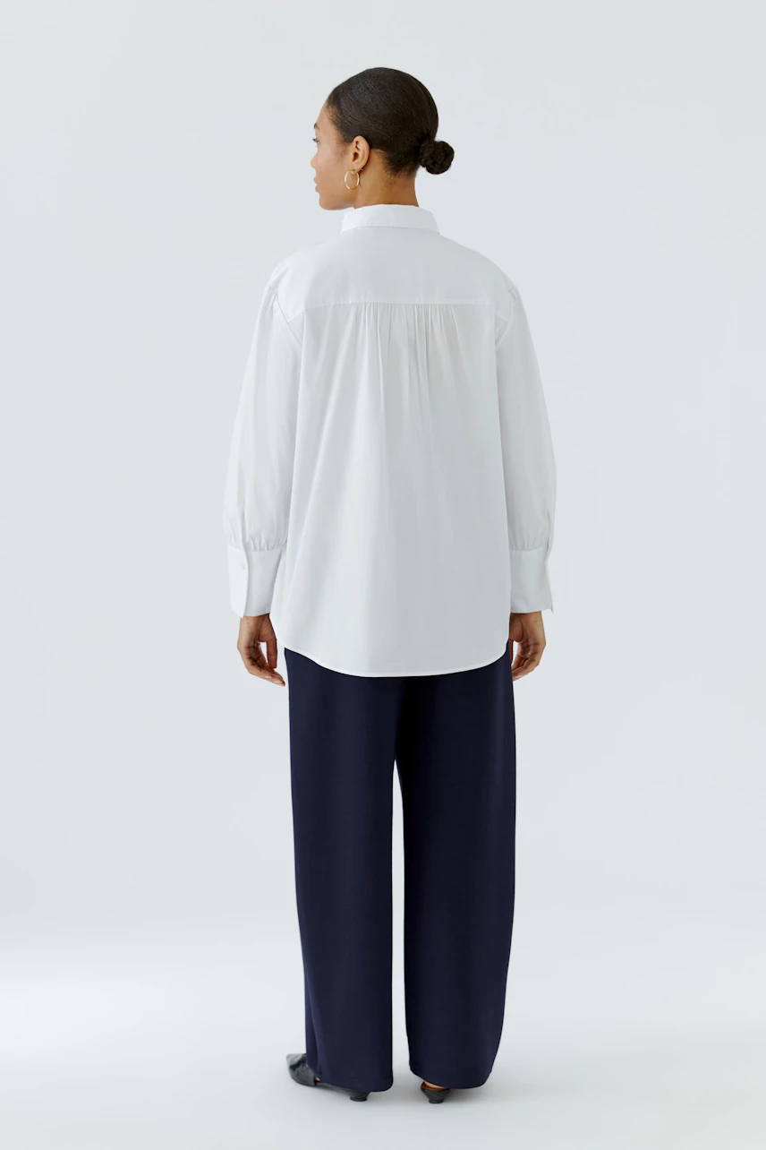 Casual women's shirt blouse: Woman in white blouse and navy pants, viewed from the back.