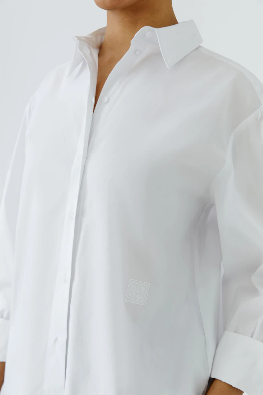 White shirt blouse: Woman in crisp white blouse with open collar and relaxed fit.