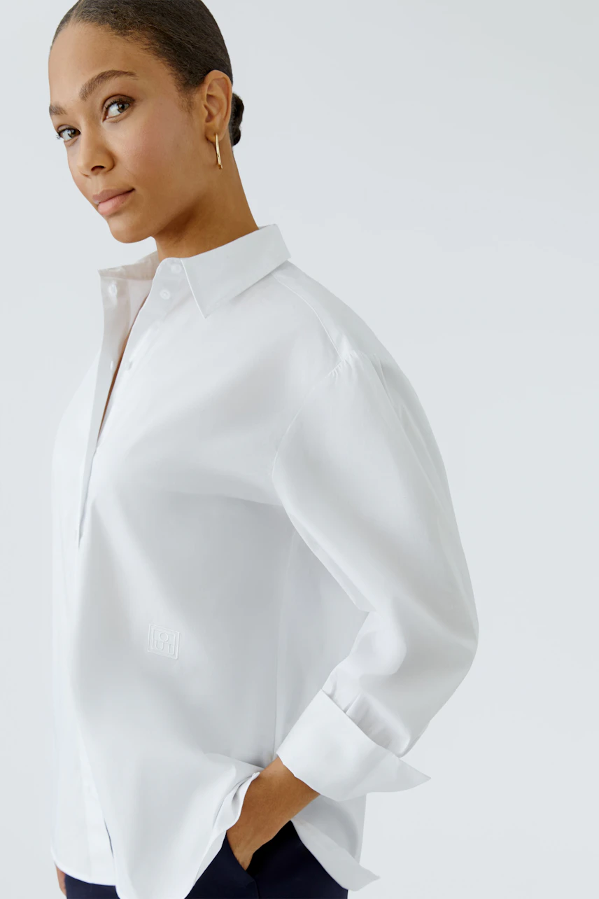 Casual women's blouse: Woman in a white shirt blouse with rolled sleeves, looking confidently.