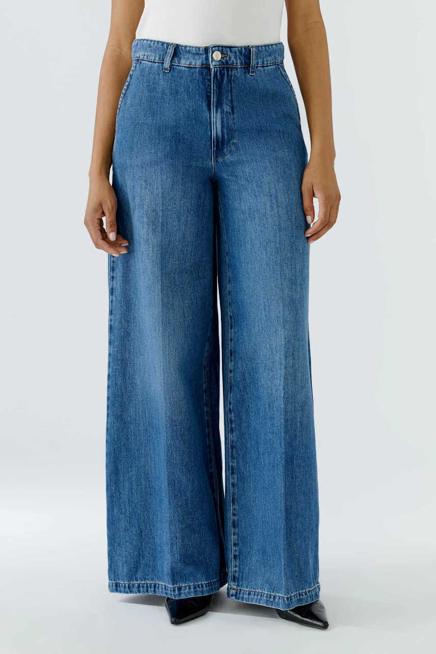 Casual wide leg jeans: Woman in blue denim wide leg jeans, white top, and black shoes.
