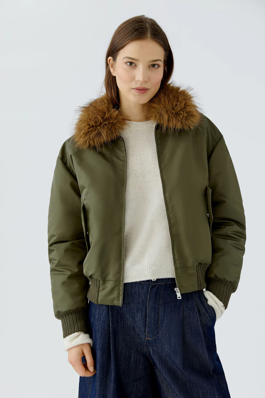 Casual blouson: Woman in olive green blouson with fur collar, cream pullover, and blue jeans.