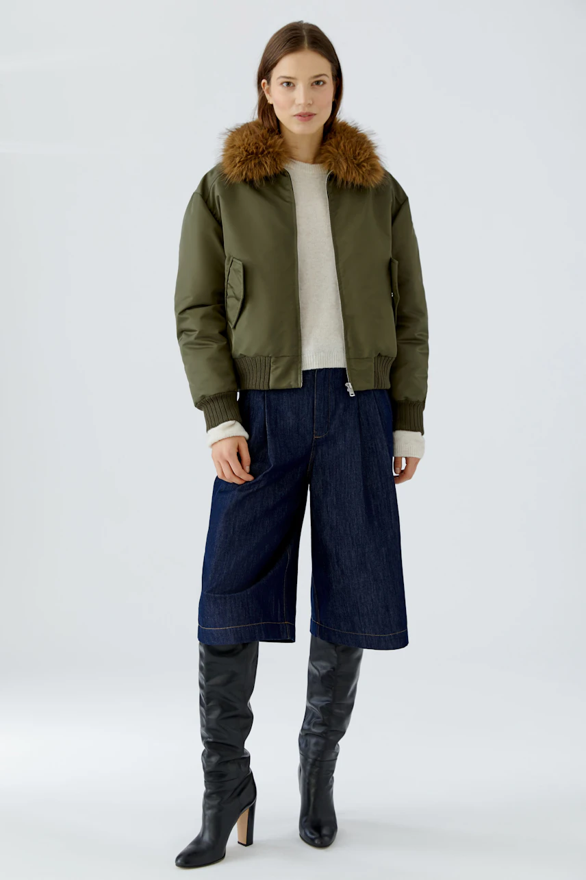 Casual blouson: Woman in olive blouson with fur collar, denim culottes, and knee-high boots.