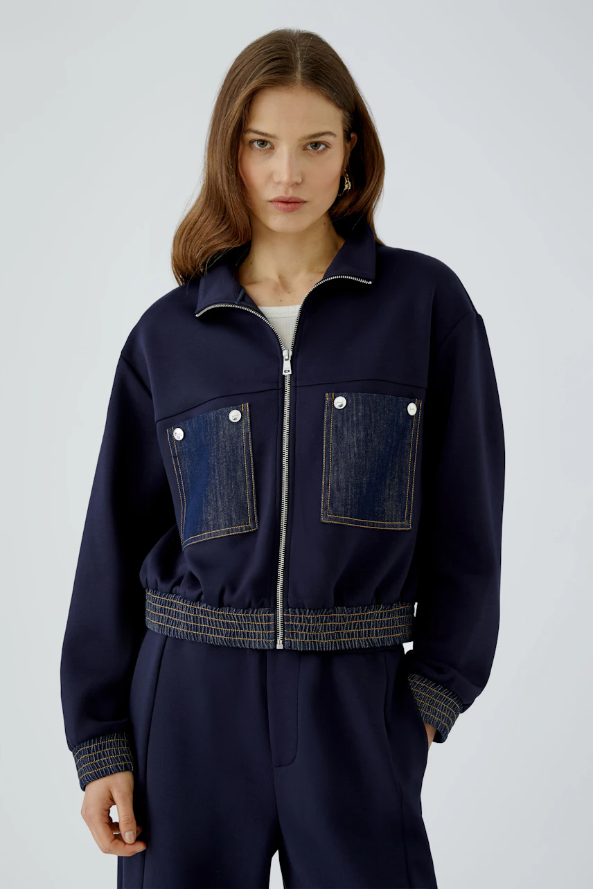 Casual blouson: Woman in navy blouson with denim pockets, standing confidently.