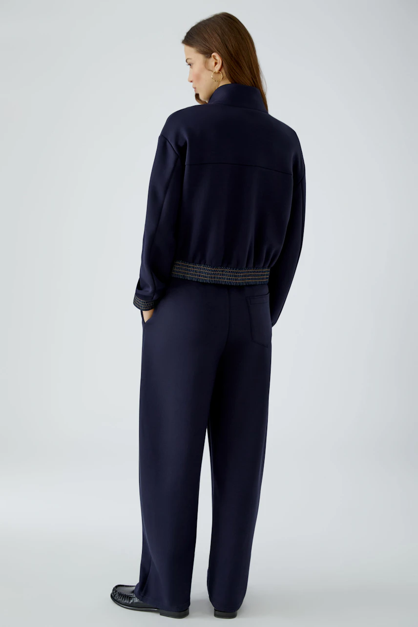 Woman in navy blouson and matching pants, standing with hands in pockets, showcasing casual style.