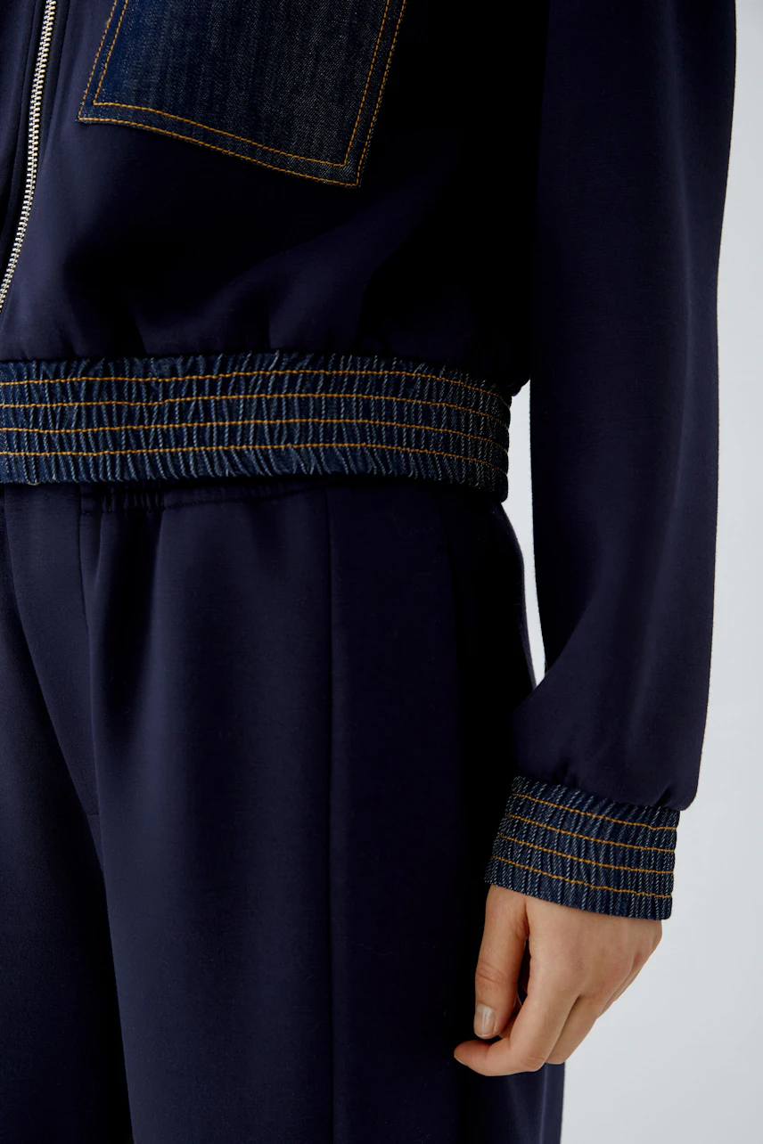 Navy blouson with denim accents, worn by a woman. Features elastic cuffs and waistband for a relaxed fit.