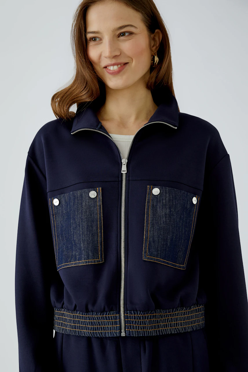 Casual blouson: Woman in navy blouson with denim pockets, smiling confidently.