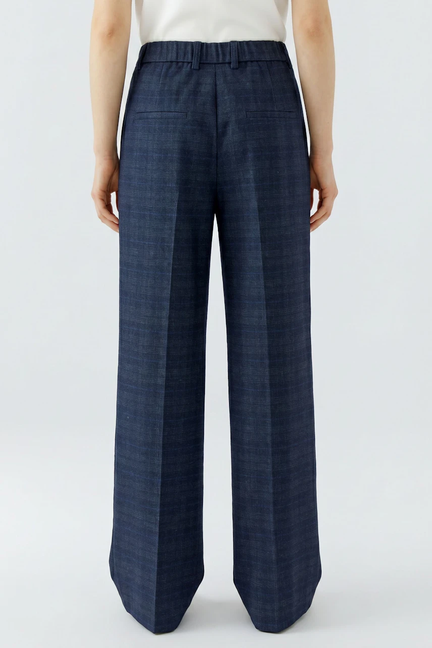 Women's trousers: Woman in wide-leg navy trousers, standing, showcasing back view.